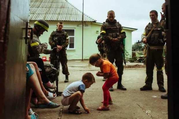 Українські військові дивляться, як грають діти в одному з донбаських дворів
