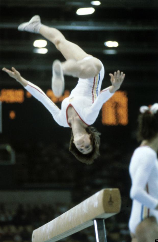 Румунська гімнастка Надя Команечі виконує «перекид» під час виступу, за який вона отримає чергову ідеальну десятку, на цей раз на балансирі. Її перші круглі 10 балів були присуджені на Олімпіаді в Монреалі в 1976 році. Вона стала першою гімнасткою в історії, яка досягла такого результату