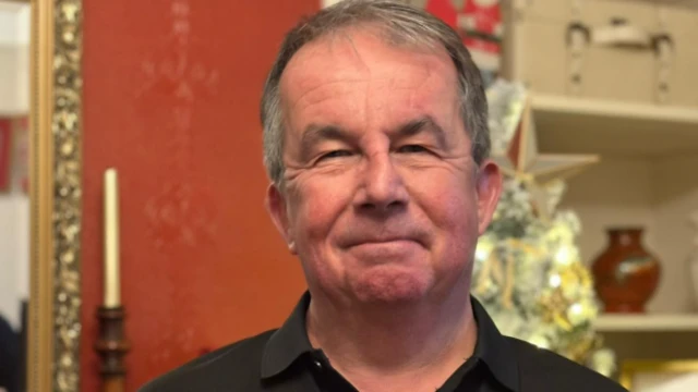 Чоловік років 60 із сивим волоссям, одягнений у чорну футболку-поло